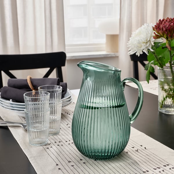 Glass water jug and drinking glasses on a dining table.				