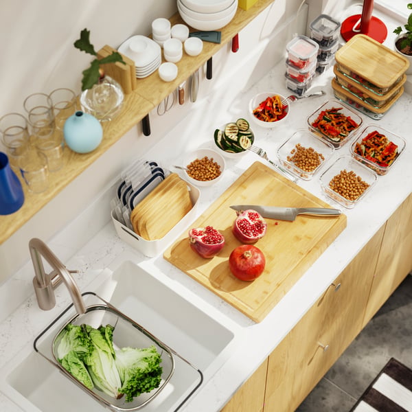 An bird-eye’s view of a kitchen worktop with a cutting board and several food containers, where meals are being prepared.
