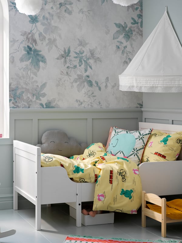 A SUNDVIK extendable bed with colourful bed linen stands in a corner. A LEN bed canopy is attached to the wall above.
