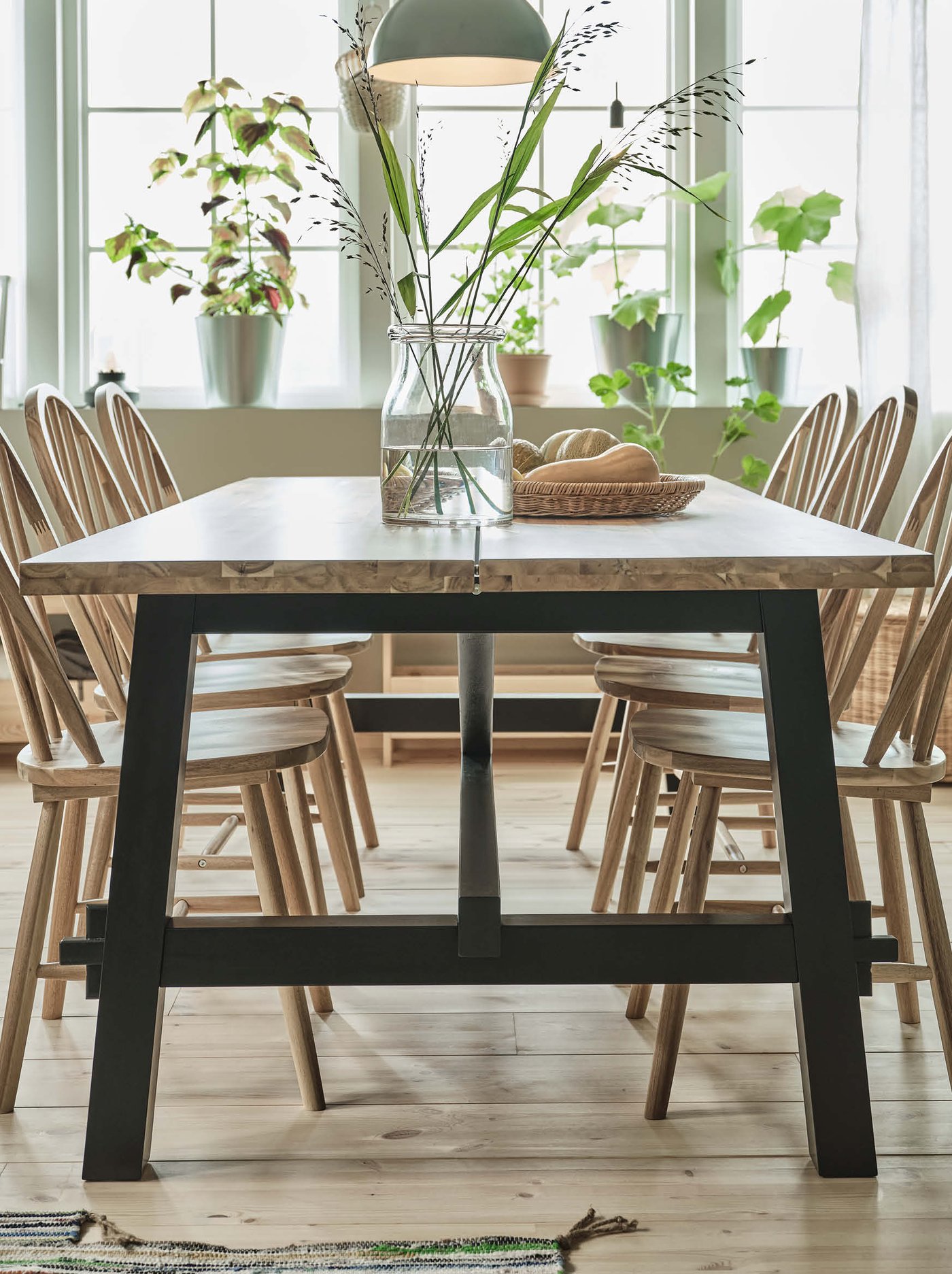 Une table de salle à manger en bois SKOGSTA et six chaises SKOGSTA se trouvent dans une pièce à manger sous deux lampes suspendues SKURUP.