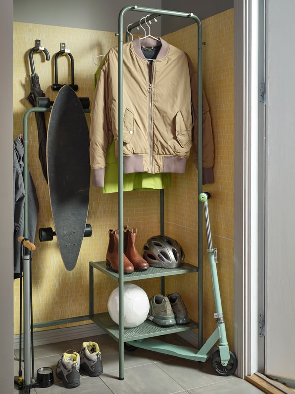A hallway with a NIKKEBY clothes rack holding clothing, footwear and a skateboard. Hooks hold various objects nearby.