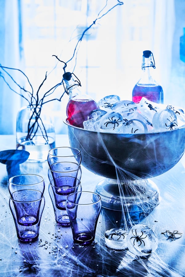 Ein von Halloween inspirierter Tisch mit Getränken in KORKEN-Flaschen mit Verschluss in einer großen Schüssel mit Eiswürfeln mit Plastikspinnen auf einem Tisch mit Tassen und Spinnennetzen.