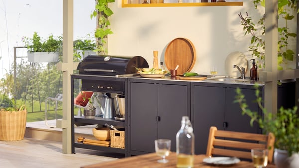 A GRILLSKÄR outdoor charcoal barbeque and kitchen island in black stainless steel with grilling and cooking accessories.