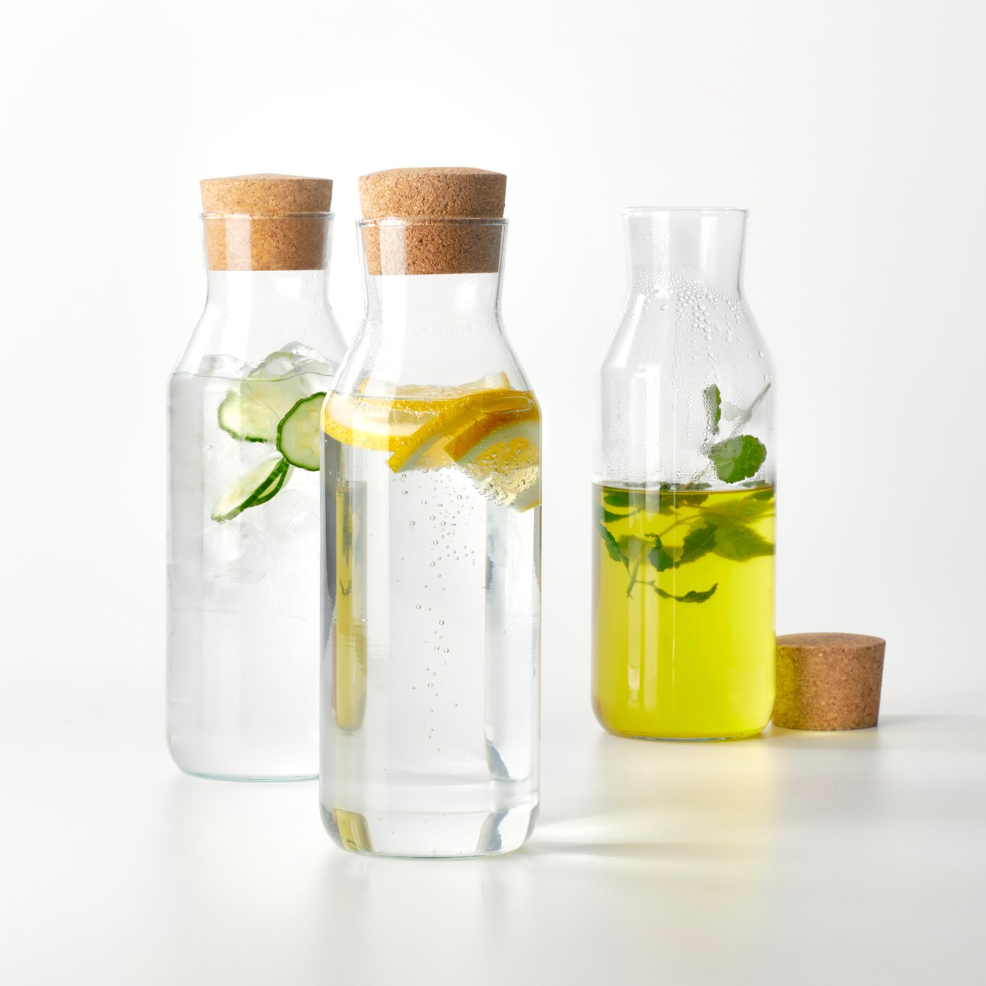 Trois carafes en verre IKEA 365+ avec bouchon en liège. L'une contient du thé chaud, une autre de l'eau glacée et la troisième de l'eau pétillante.
