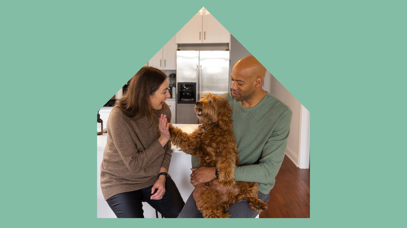 A large house shape with image of a young couple sitting in their kitchen laughing and playing with their small dog.