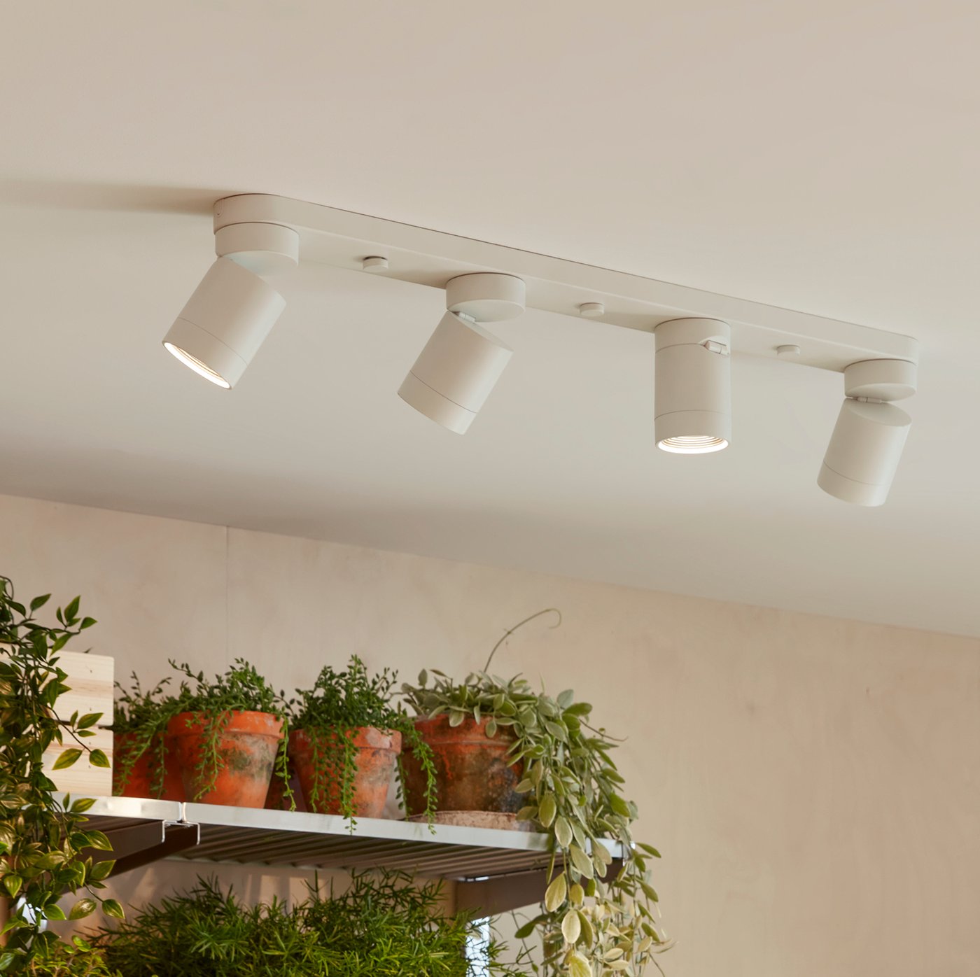 Lámparas de techo blancas de cuatro NYMÅNE junto a mueble con maceteros con plantas.