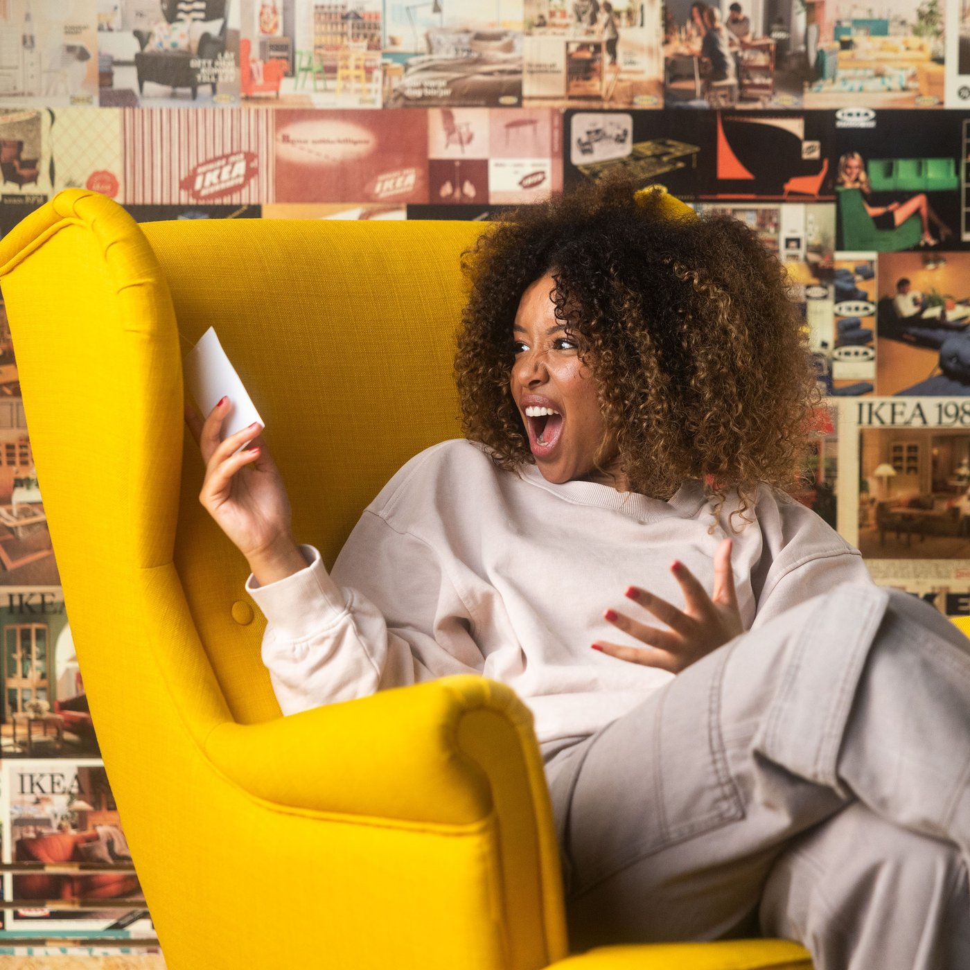 A woman sits in a large yellow chair and looks happily at a price tag.