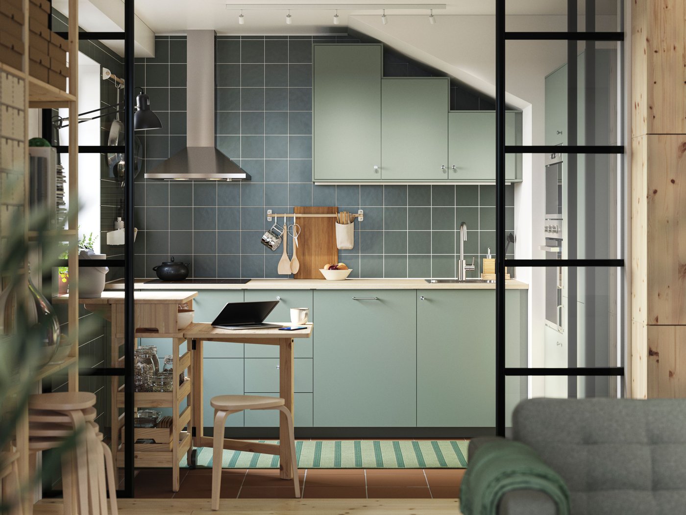 A green L-shaped kitchen has grey green NICKEBO fronts and a RESARÖ mobile drop-leaf table with storage and some stools.