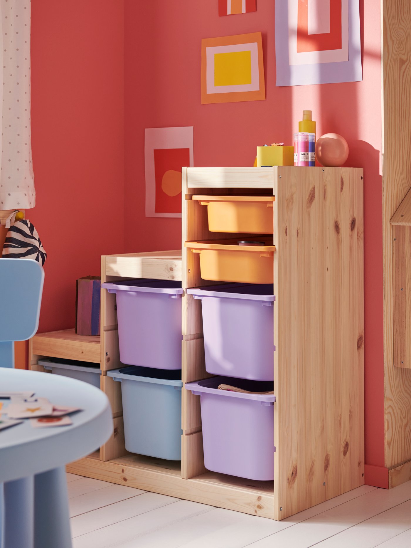 A light white stained pine TROFAST frame holding storage boxes in lilac, light blue and light orange in a children’s room.