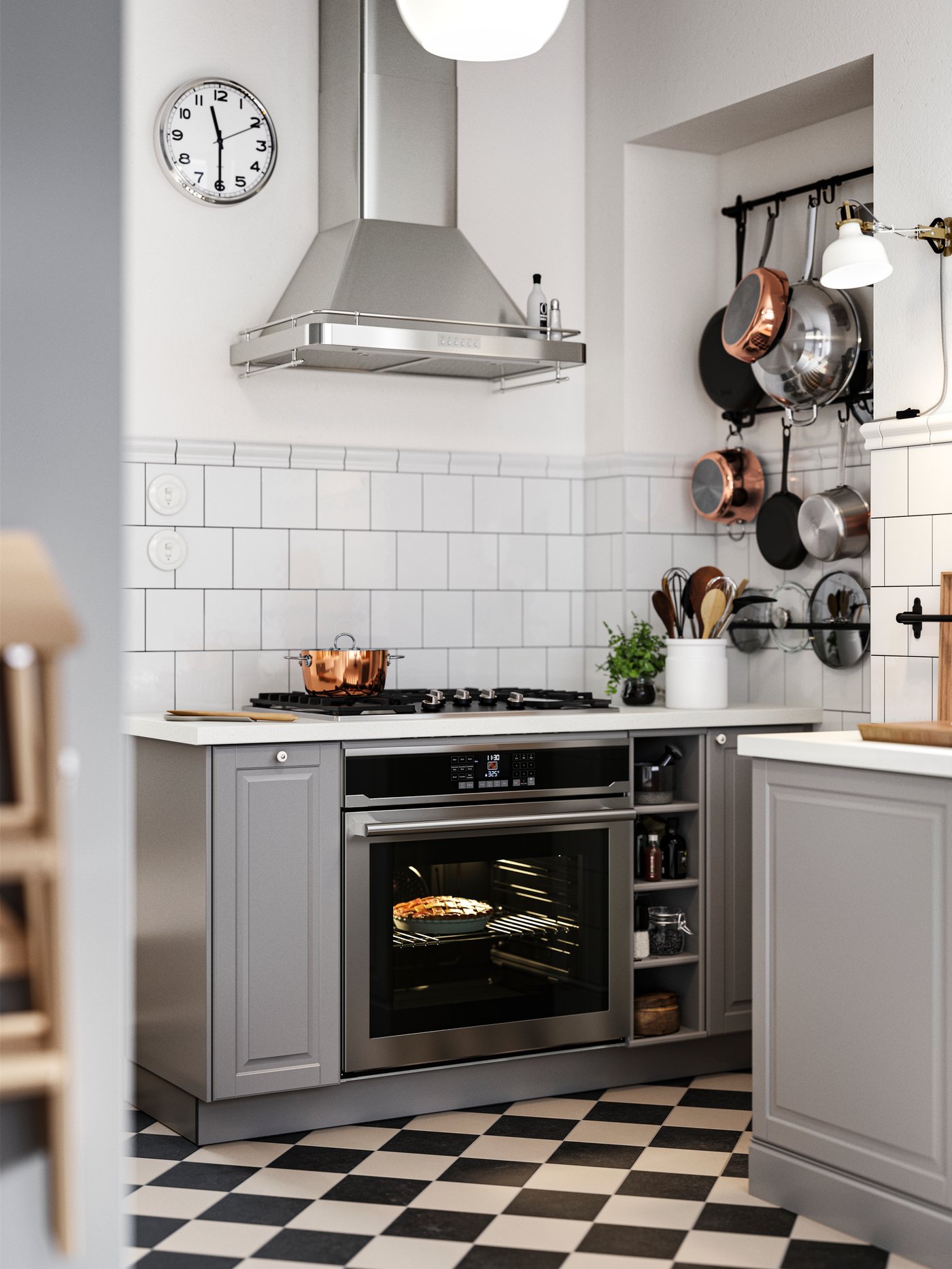 Es sind Unterschränke mit grauen BODBYN Fronten zu beiden Seiten eines Kochfelds mit Backofen und schwarze Stangen an der Wand zu sehen, an denen Töpfe und Pfannen hängen.