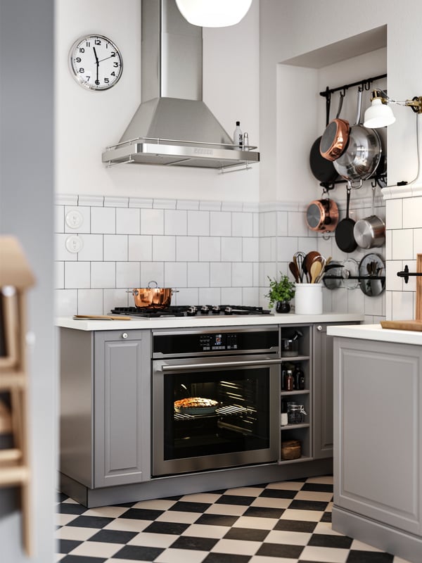 Base cabinets with grey BODBYN kitchen fronts on both sides of a hob and oven, plus black wall rails holding pots and pans.