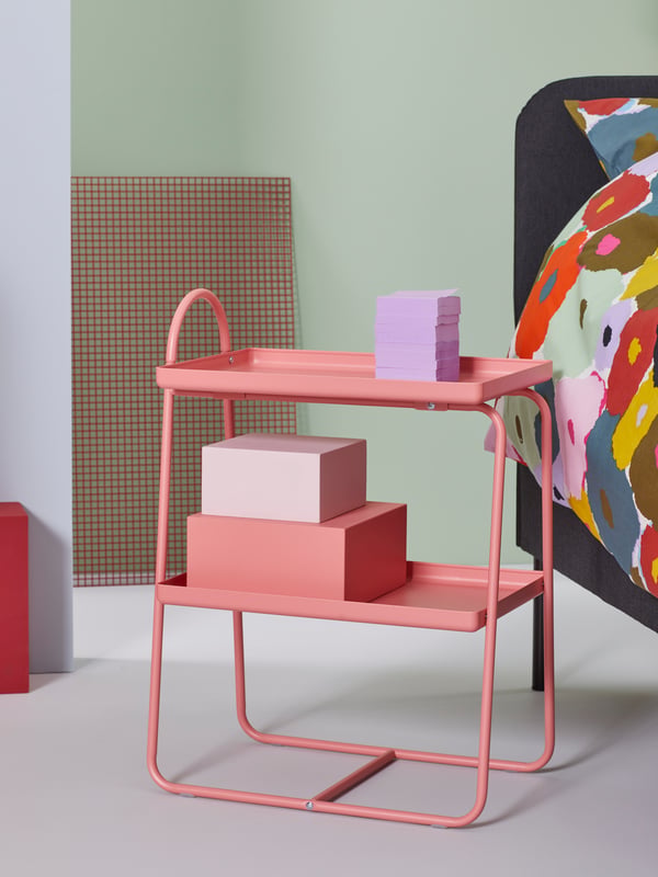 Un comodino/scaffale IKEA rosa su cui sono appoggiati diversi accessori.