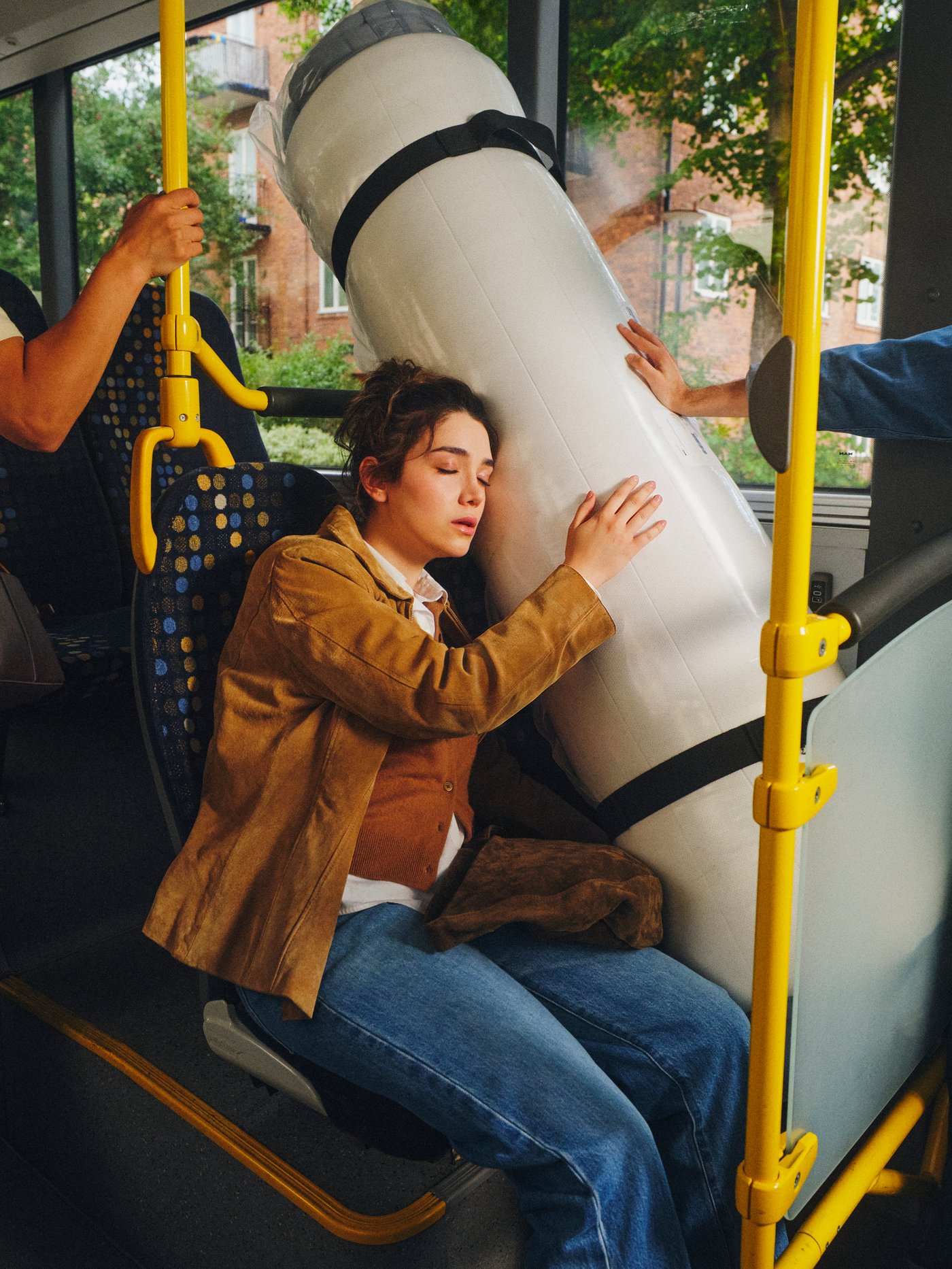 VALEVÅG dušek s oprugama u džepovima u originalnom urolanom pakovanju na sedištu autobusa pored prozora. Osoba dremka naslonjena na dušek.