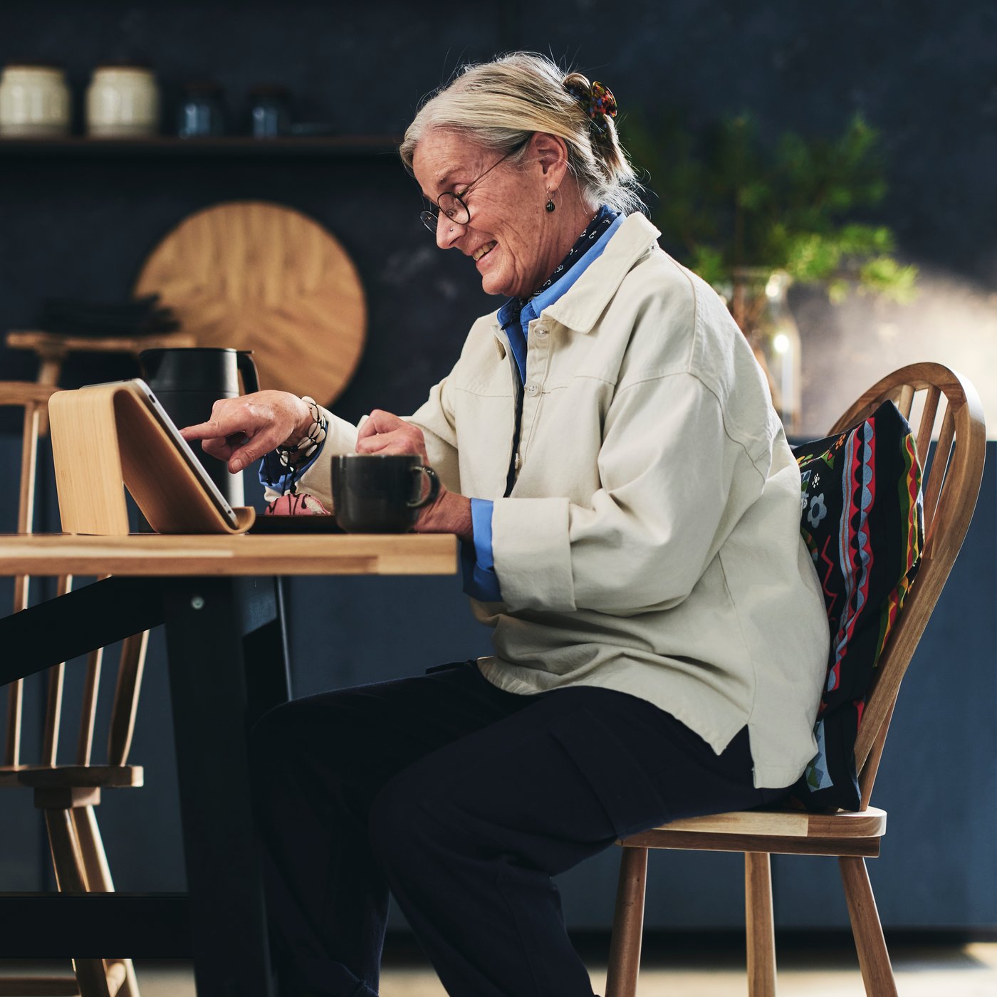 Une grand-mère assise à une table et savourant une tasse de thé tout en faisant un appel vidéo sur sa tablette.