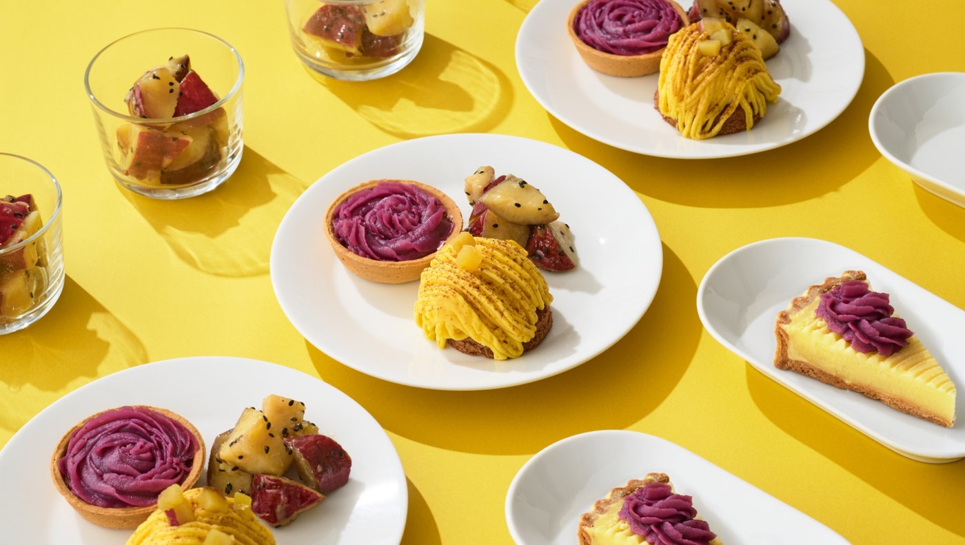 White plates and clear glasses on a bright yellow table, each with purple paste and yellow food arranged on top.