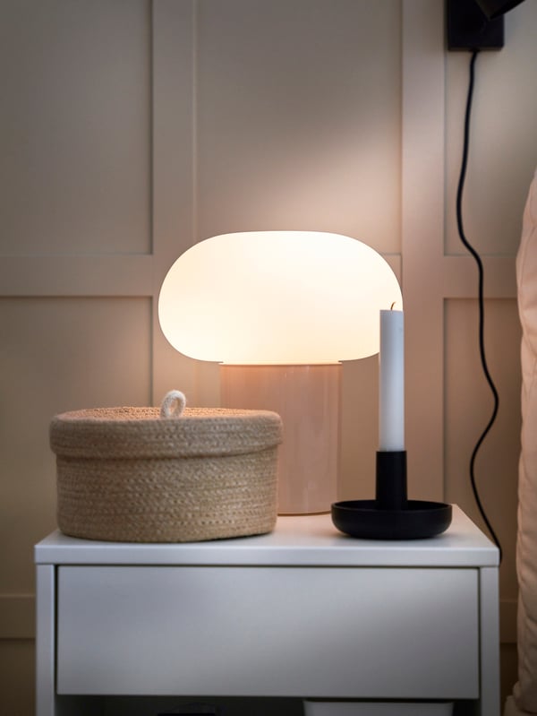 Närbild på ett sängbord med lampa och ljusstake.