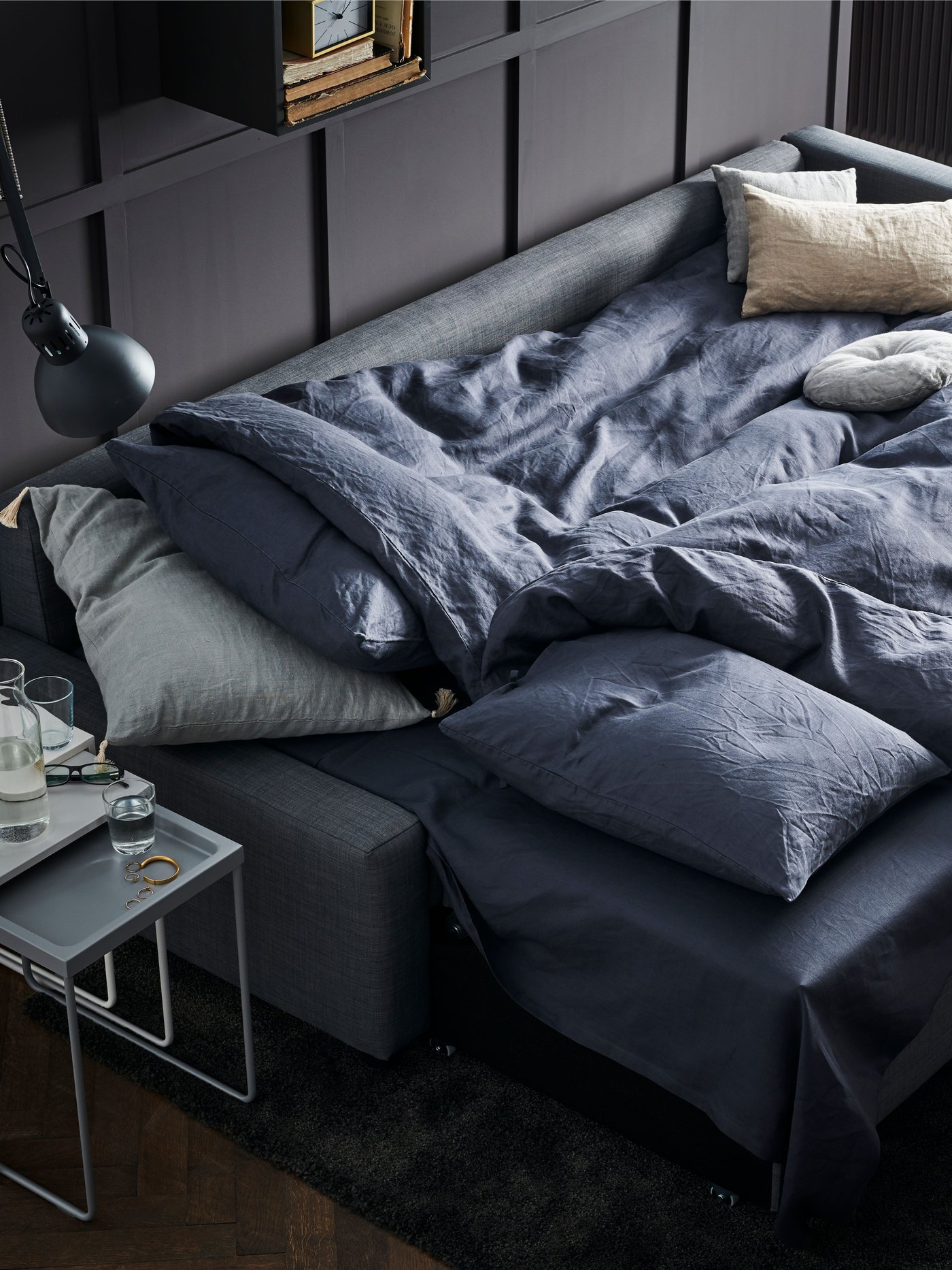 Un sofá cama FRIHETEN extendido con ropa de cama lista para dormir.