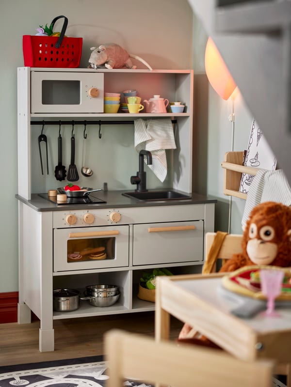 SILLTRUT kitchen for children full of toy kitchen articles, and an orangutang soft toy waiting to be served by the table.