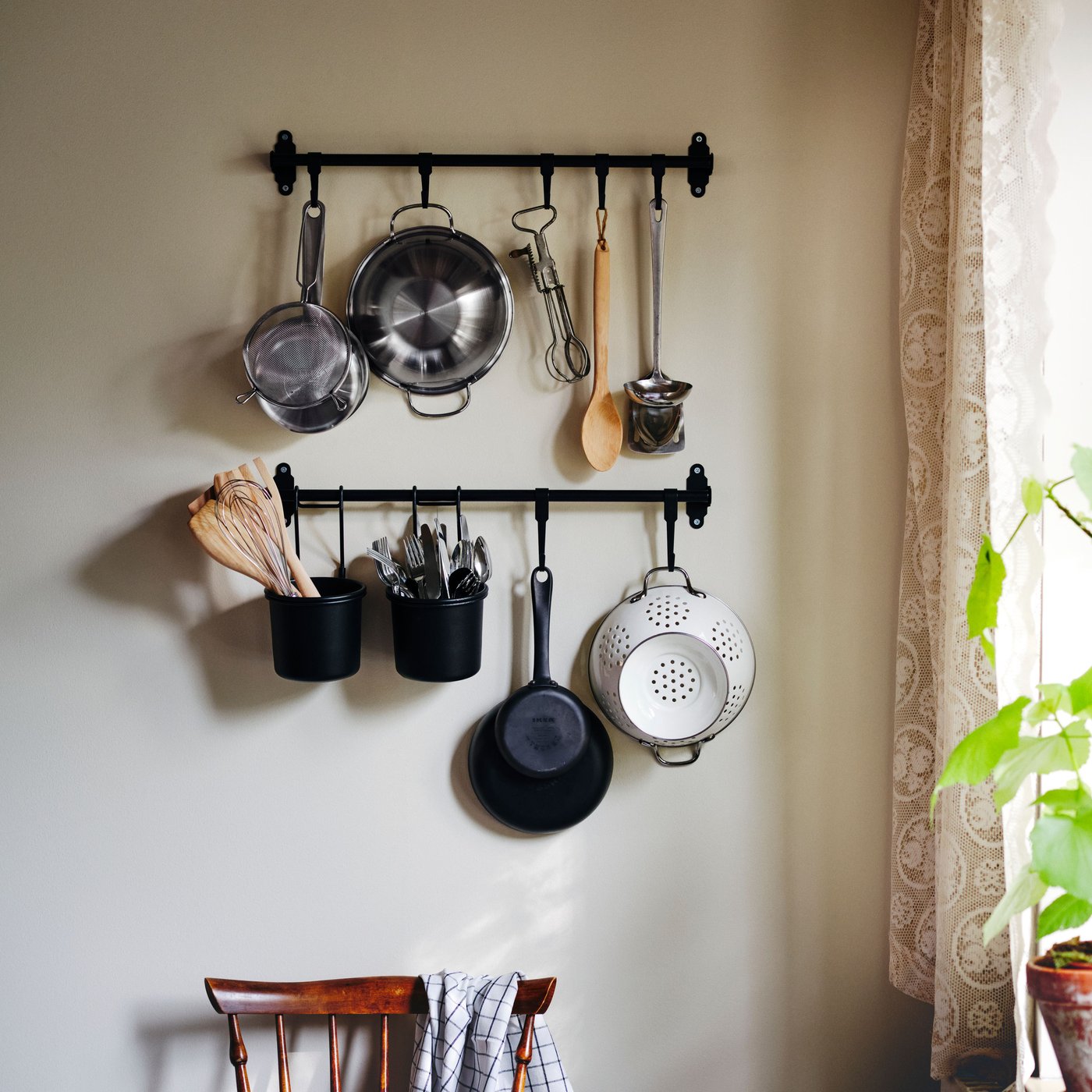 Two black HULTARP rails with hooks and containers holding a saucepan, colander, strainer and various kitchen utensils. 
