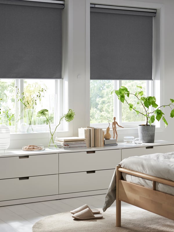 Ein IKEA FYRTUR Verdunklungsrollo kabellos/batteriebetrieben grau wird mit einer batteriebetriebenen Fernbedienung abgesenkt.