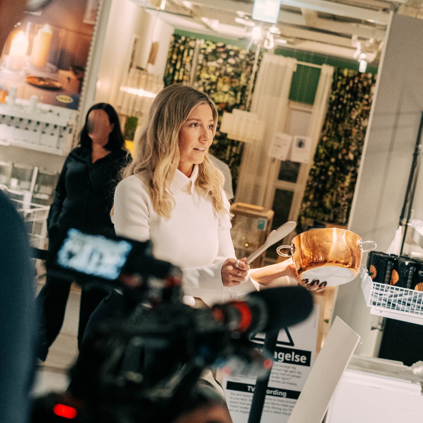 En optagelse fra "Hvem vinder hjem?" TV-programmet, hvor vært Carla Mickelborg holder en gryde og en grydeske mens en kameramand filmer scenen i et IKEA varehus.