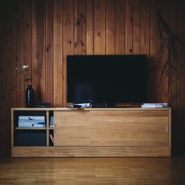Auf einer TONSTAD TV-Bank mit Türen aus Eichenfurnier sind ein Fernseher und eine Vase platziert.