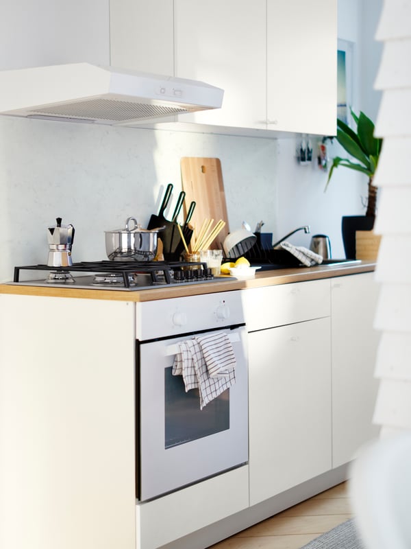 A white KNOXHULT kitchen with a LAGAN extractor hood. A knife stand and chopping board stand on the kitchen worktop.
