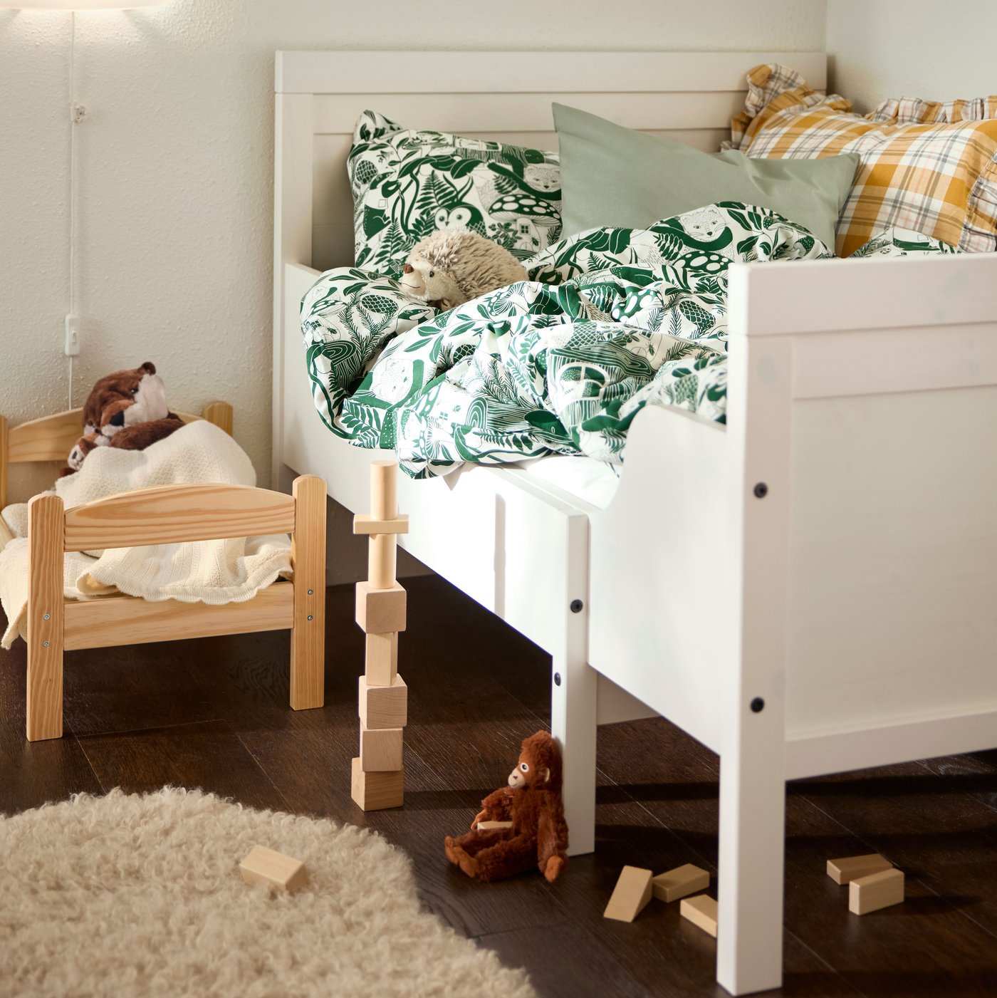 Close-up of SUNDVIK extendable bed with DUKTIG doll’s bed and some scattered toys on the floor next to it.