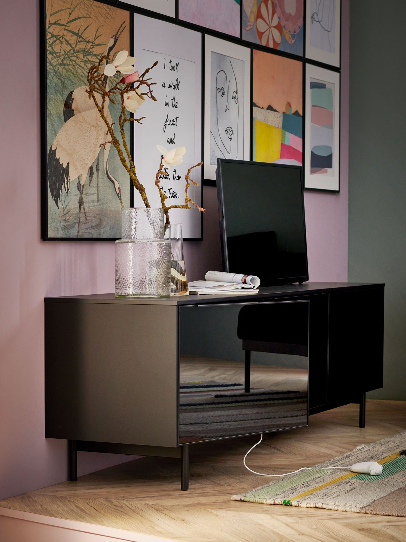 Banc TV avec tiroirs RANNÄS avec un vase et un téléviseur posés dessus, installé contre un mur orné de nombreuses affiches BILD.