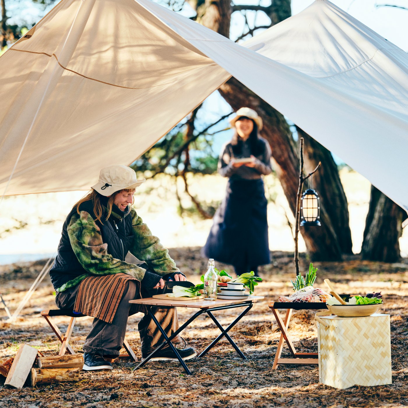 Two persons are in a campsite with a SOLUPPGÅNG folding table made, set up for a meal under the canopy.