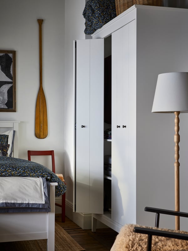 Beli IDANÄS garderober stoji u uglu spavaće sobe pored KINNAHULT podne lampe boje jasena/bele boje i HEMNES kreveta.