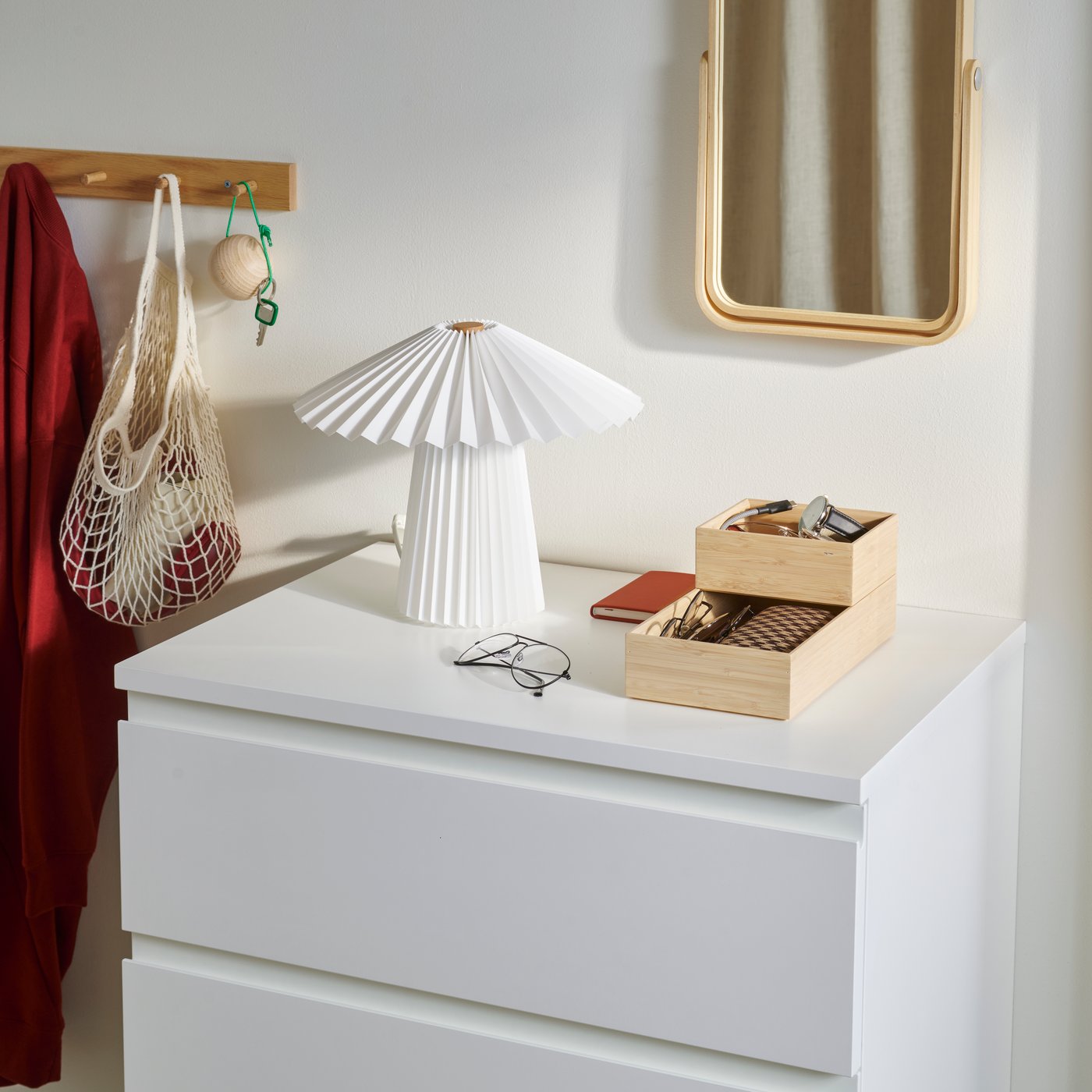 A white STORKLINTA chest of 4 drawers with MALVA table lamp, 2 STEGESUND boxes and IKORNNES table mirror arranged on top.