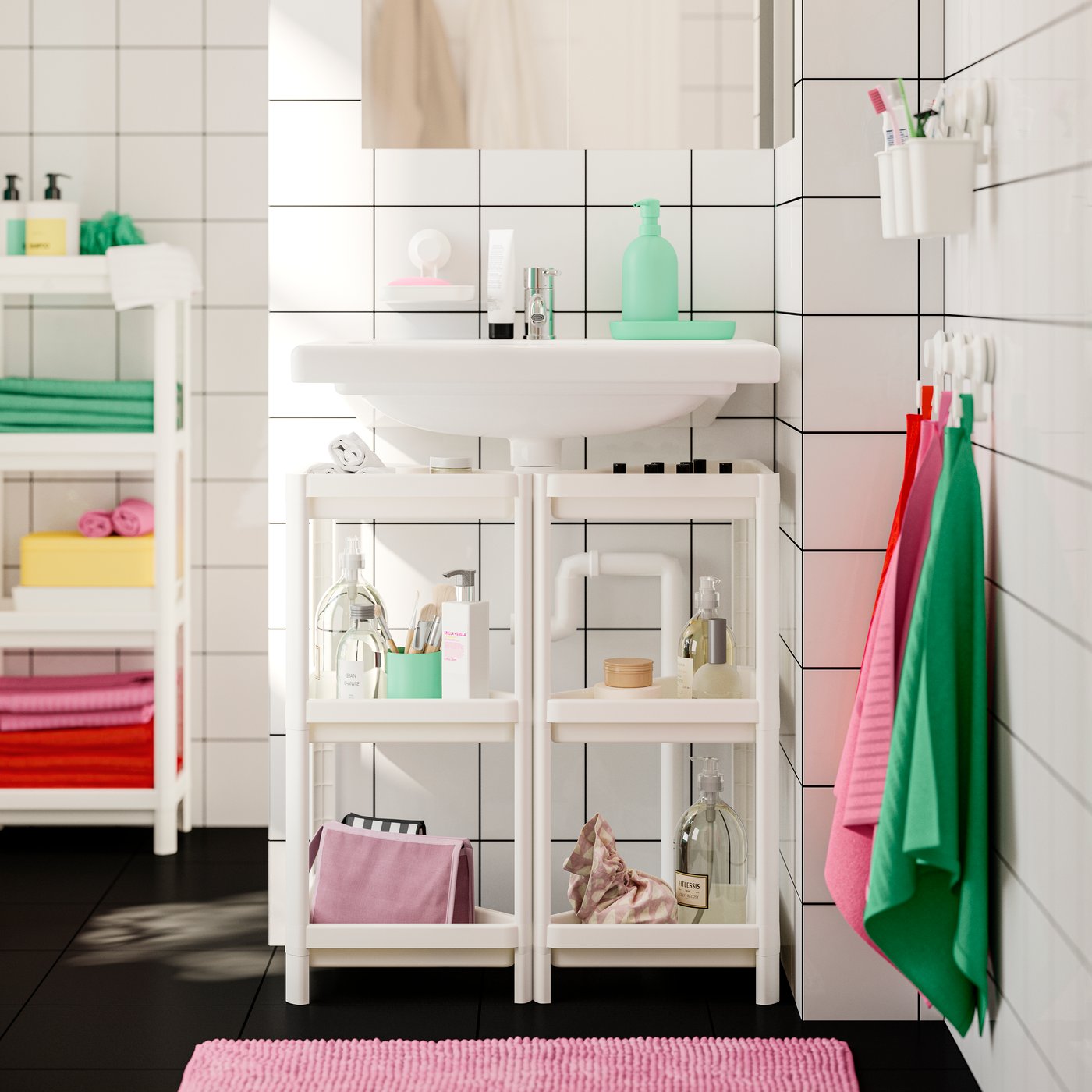 n einem Badezimmer sind zwei VESKEN Eckregale mit Toilettenartikeln unter einem Waschbecken zu sehen. An der Wand hängen rosafarbene und grüne Handtücher.