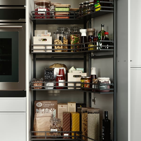 A pantry with UTRUSTA pull-out larder, neatly filled with jars, bottles, pasta, sauces, and wooden boxes on the shelves.