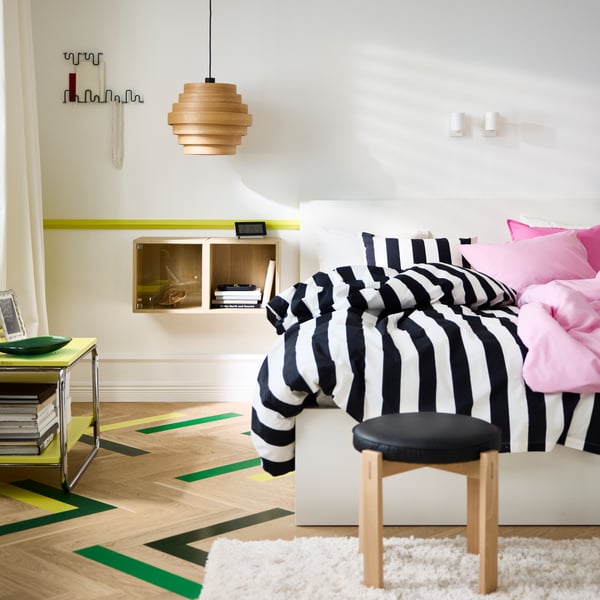 Bedroom with white walls and a double bed with black/white striped bedding to the left and bright pink to the right.