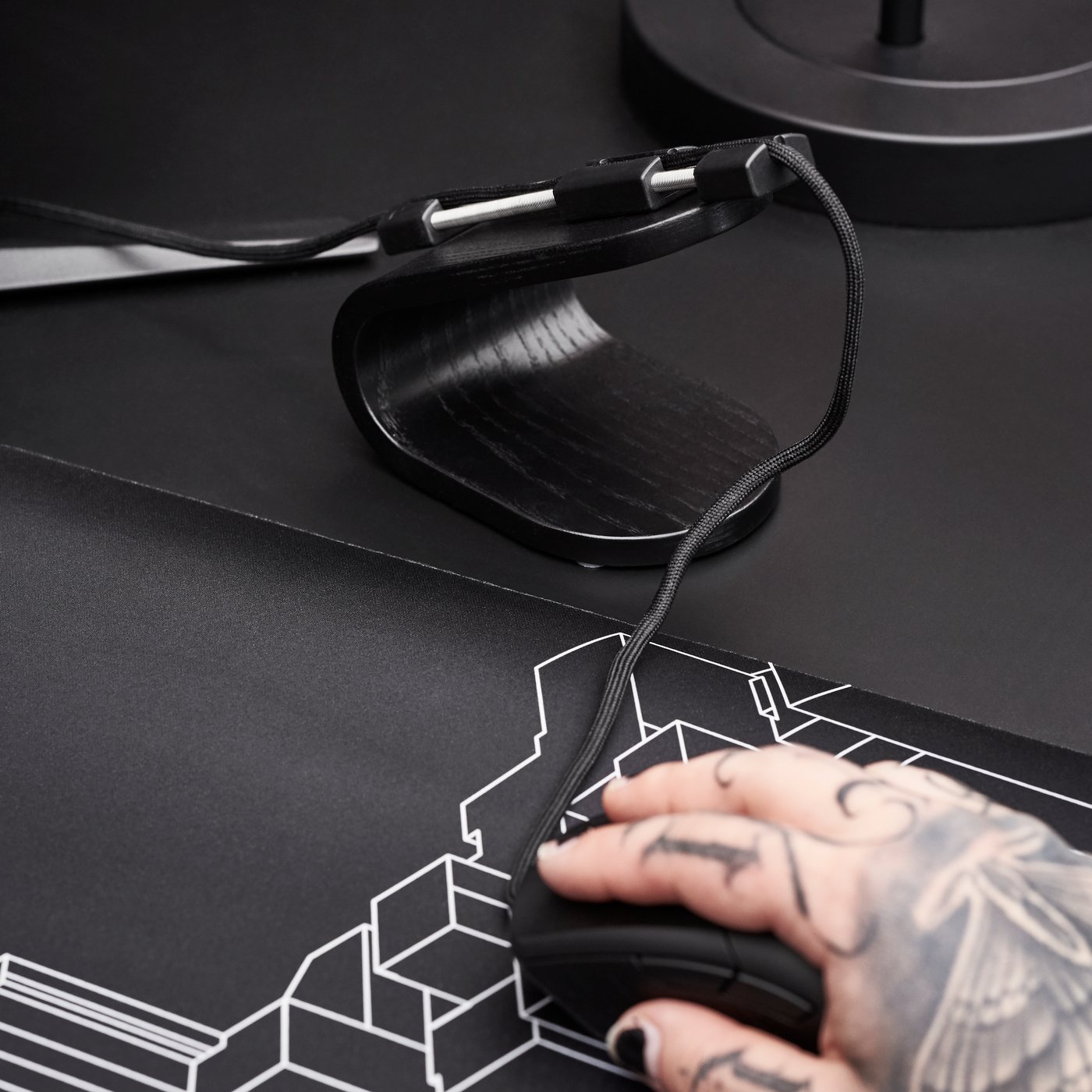 A tattooed hand holding a mouse next to a LÅNESPELARE mouse bungee.