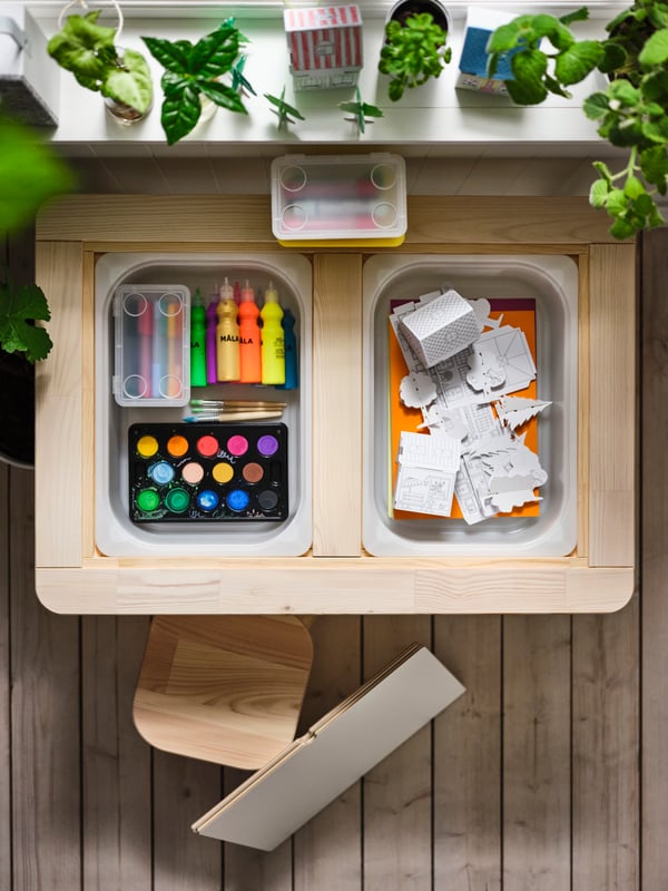 A FLISAT children’s table, insets off, revealing compartments with MÅLA mixed colours and cardboard-town templates inside.