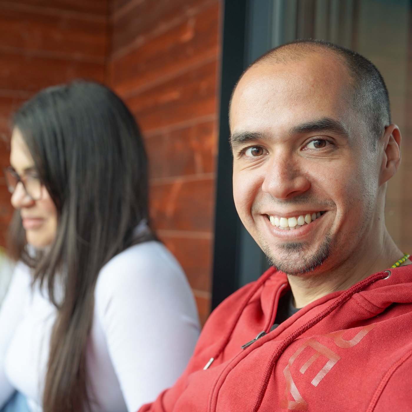 Edgar sits outdoors in his red shirt and smiles at the camera.
