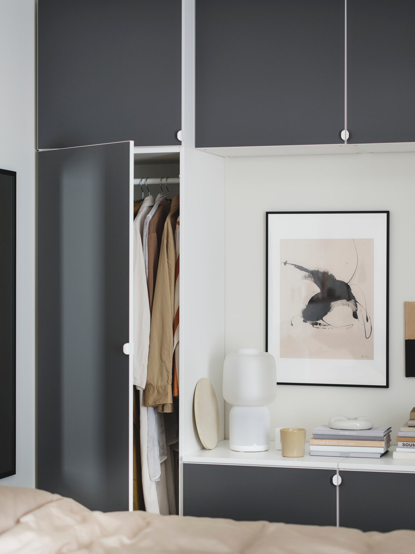 A PLATSA wardrobe combination in grey with an open door filled with clothes. A mirror and a lamp are placed next to it.