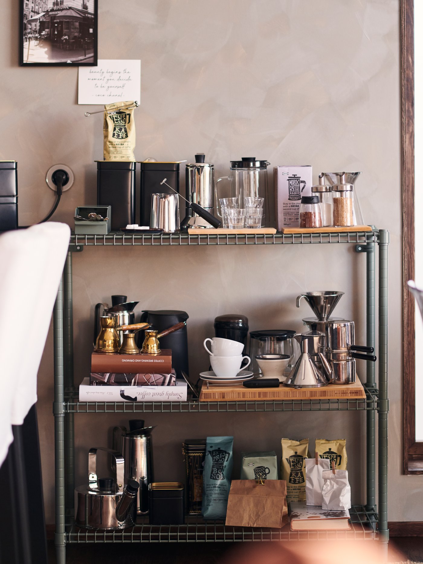 An OMAR shelving unit against a beige wall holding coffee pots, cups, saucers, coffee and other coffee-making accessories.