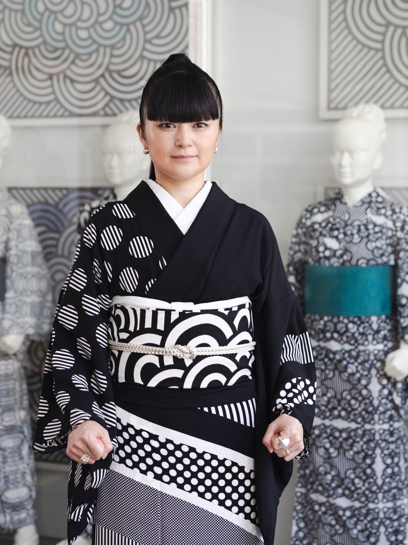 Designer Hiroko Takahashi standing in front of mannequins wearing kimonos in graphic patterns.