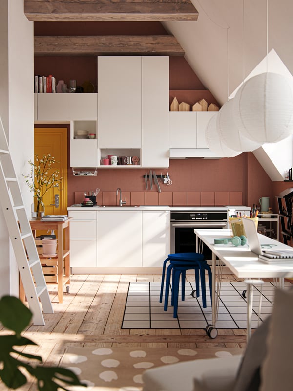 A studio apartment with sloped walls, large windows, dark walls, yellow front door and white VALLSTENA kitchen fronts.