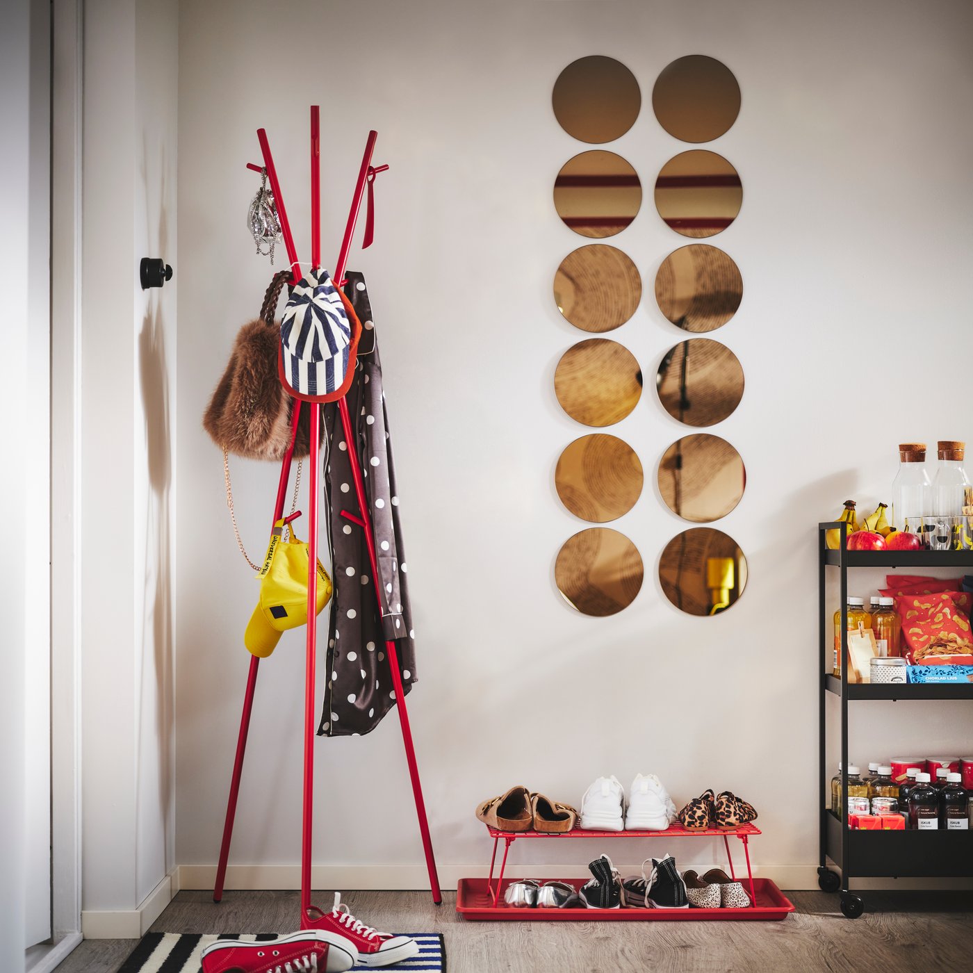 A red EKRAR hat and coat stand, GREJIG shoe rack and BAGGMUCK shoe mat beside a door hold outdoor wear, bags and shoes.