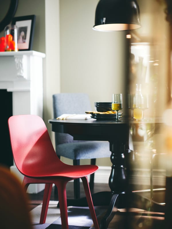 Une suspension SVARTNORA noire au-dessus d’une table extensible INGATORP noire avec une chaise ODGER rouge et une chaise BERGMUND.