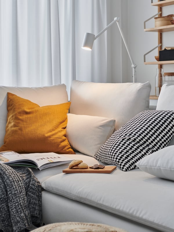 White reading lamp placed behind a beige sofa with pillows on top.