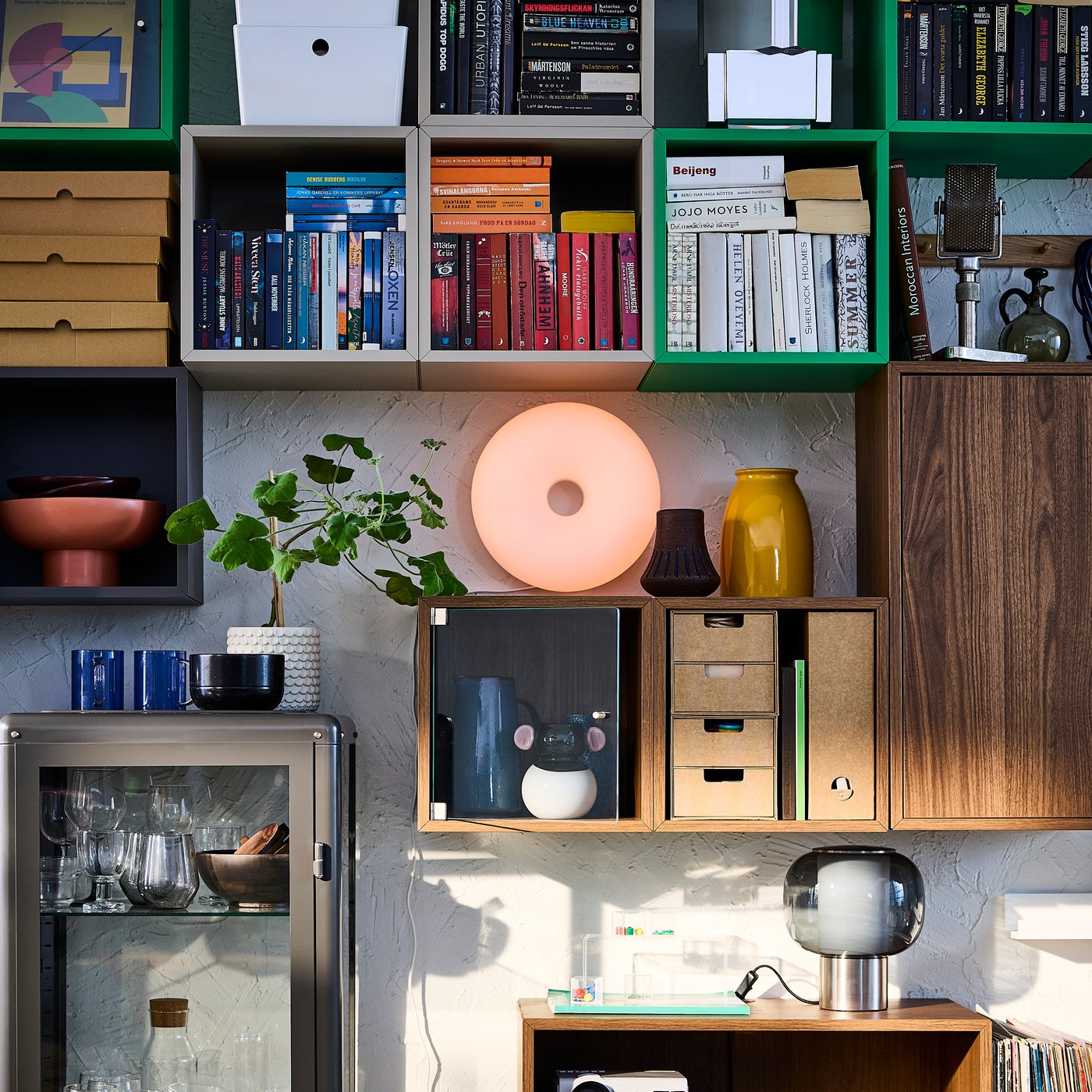 A living room wall filled with EKET cabinets in different colours, drawers and boxes for organisation, books and decorations.