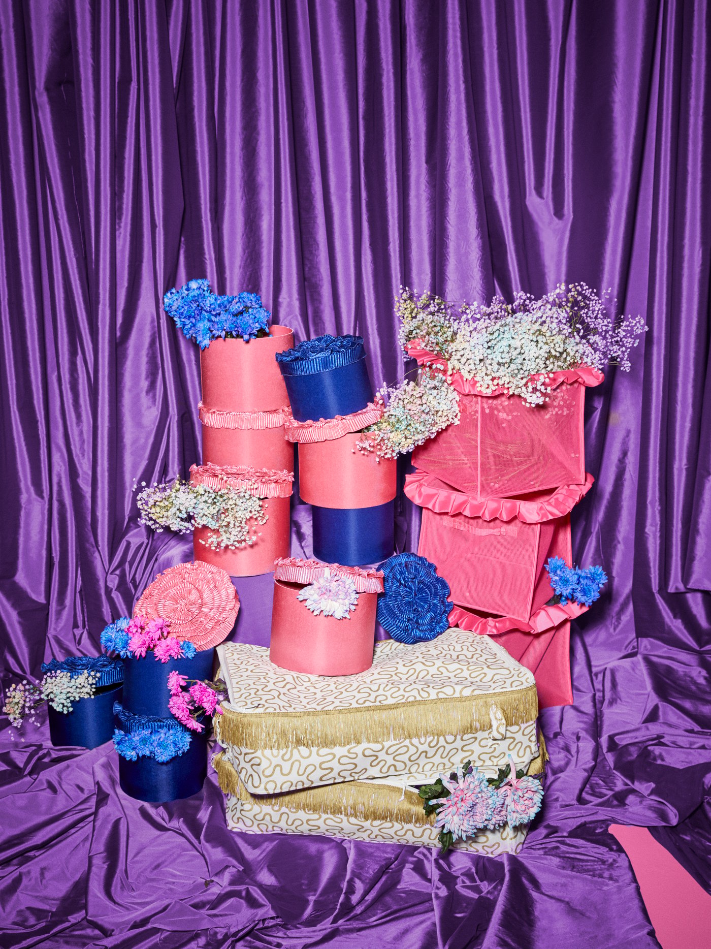 Pink and blue KARISMATISK boxes and gold storage cases are stacked on top of each other; flowers are in the boxes.