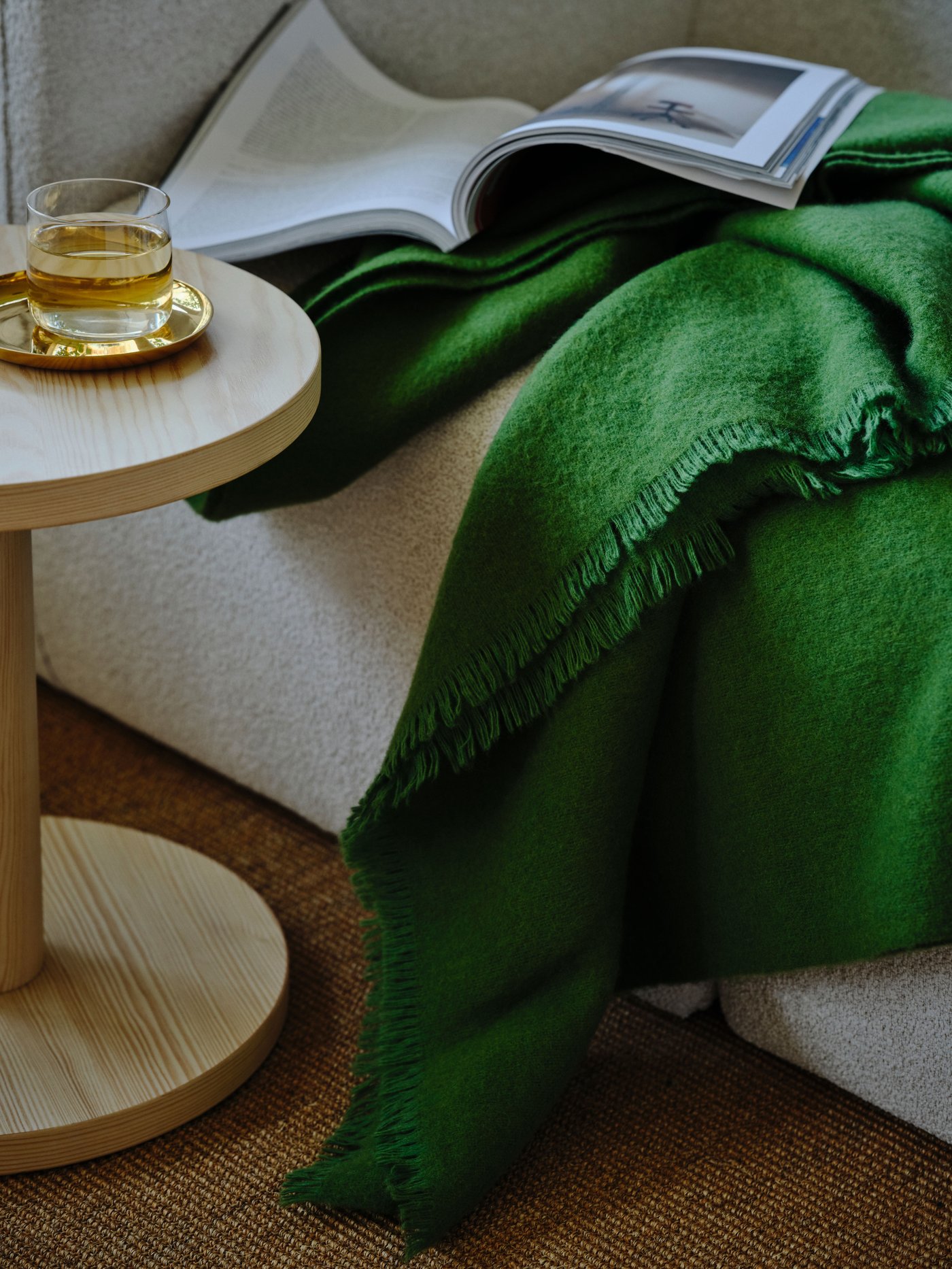 En grön STOCKHOLM pläd och en öppen katalog ligger på en ljus soffa.
