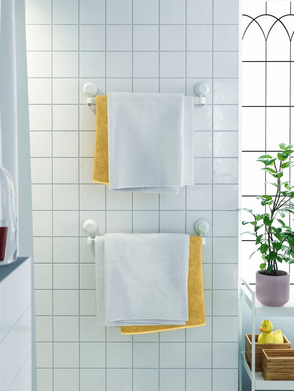 Two white towel racks with suction cups attached to a tiled wall, with white and mustard yellow towels on them.