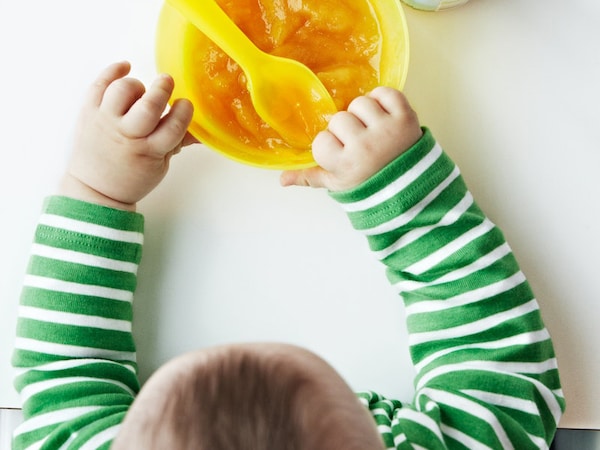 A small child sits at the table and reaches for a bowl of porridge.